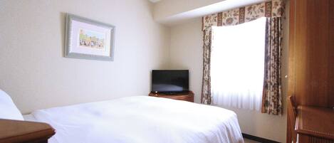 A hotel room with a large bed, a television on a wooden stand, a framed picture on the wall, and a window with curtains.