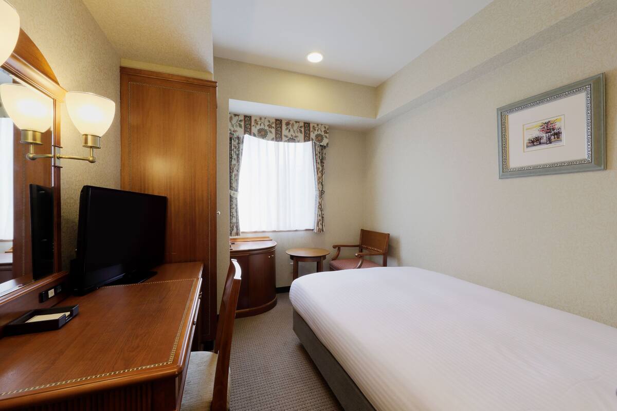 Habitación de hotel con cama, escritorio con silla, una mesita pequeña, un espejo y un cuadro en la pared.