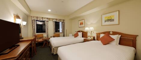 A hotel room with two beds, a desk with a TV, a chair, a desk lamp, and a window with curtains.