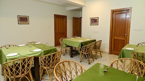 Uma área de refeições com mesas postas para quatro pessoas, cadeiras de vime e toalhas de mesa verdes.