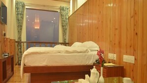 Habitación de hotel con decoración de madera, una cama con ropa de cama blanca, una mesa de vidrio con una tetera y vistas a la ciudad a través de la ventana.