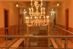 A grand staircase with a large chandelier, wooden walls, and metal railings. - Hotel Pride (Kalimpong)