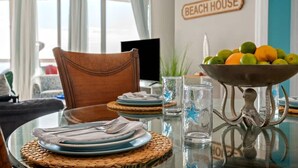 Une table à manger est dressée avec des assiettes, des couverts et un saladier rempli de fruits. Une chaise est placée à côté de la table.
