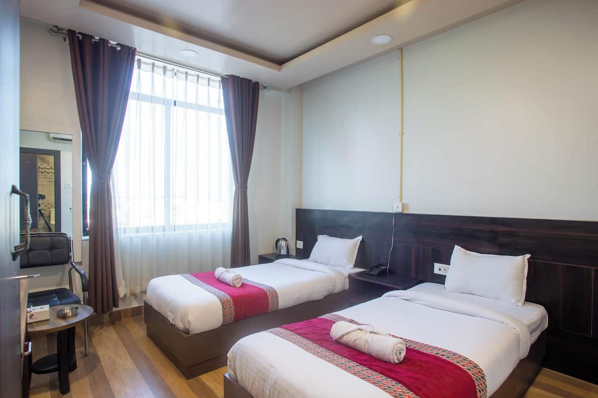 A hotel room with two beds, a desk, a chair, and a window with curtains.