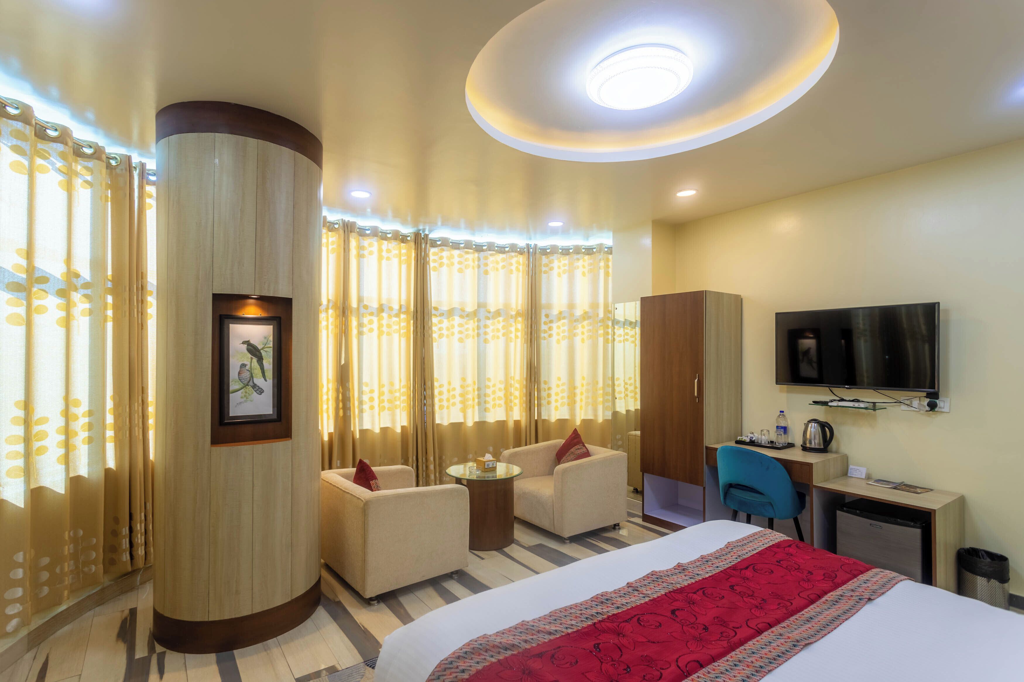 A hotel room with a bed, two armchairs, a desk, a television, and a small kitchenette.