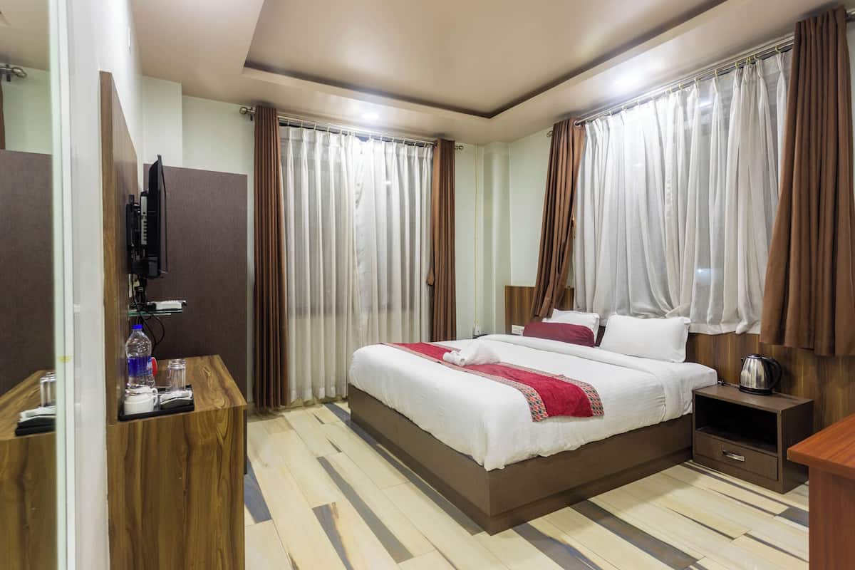 A hotel room with a large bed, a wooden desk, a television, and curtains.