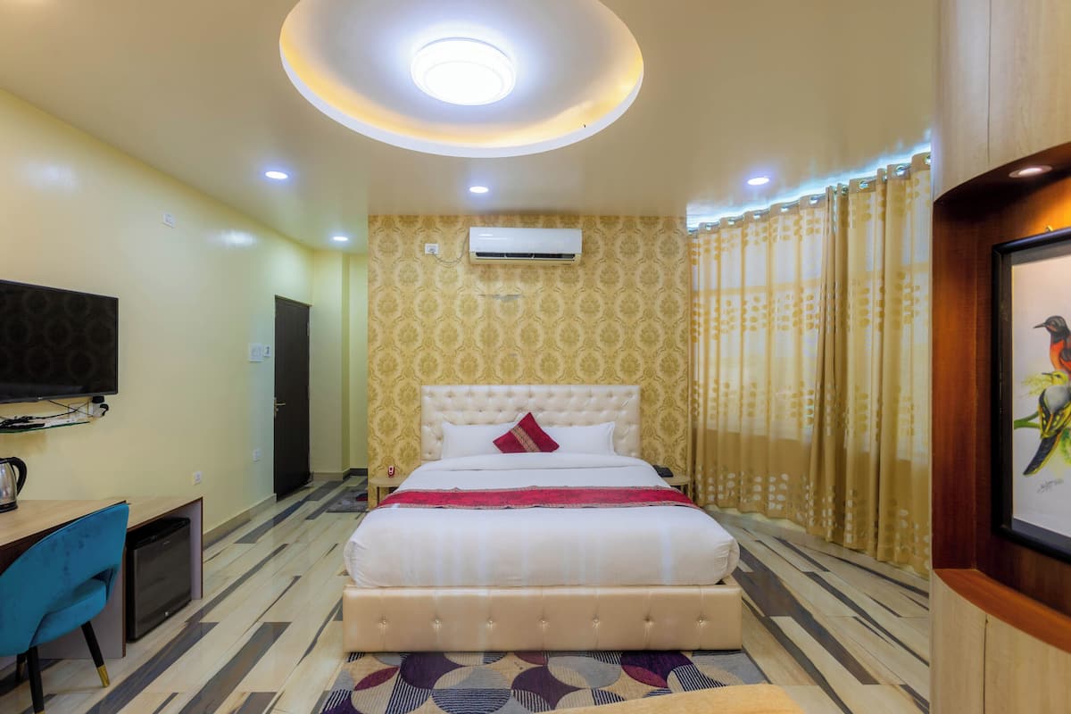 A hotel room with a large bed, a desk with a chair, a television, and an air conditioning unit.