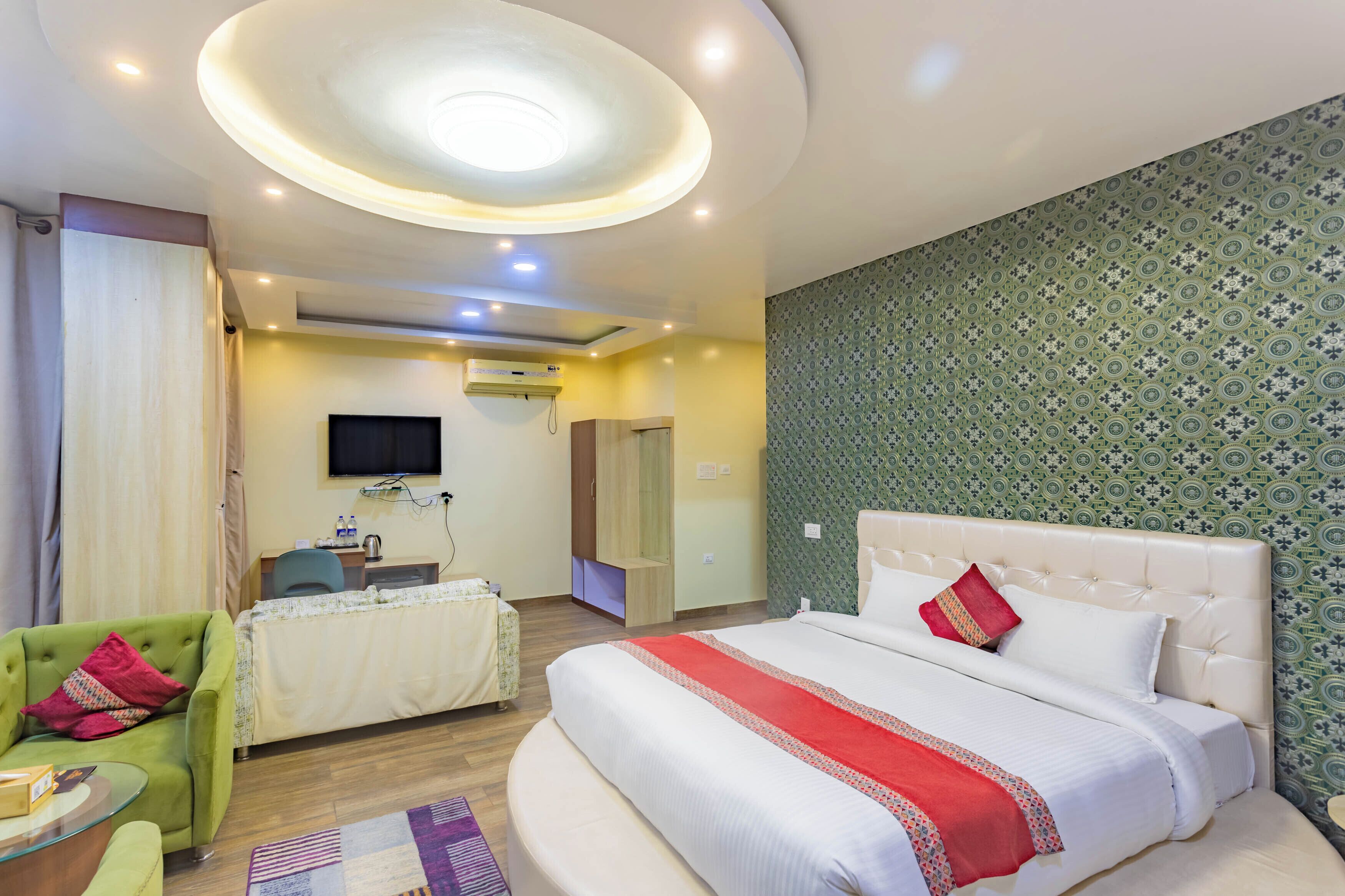 Habitación de hotel con una cama grande, un sillón verde, una mesita y un televisor en la pared.