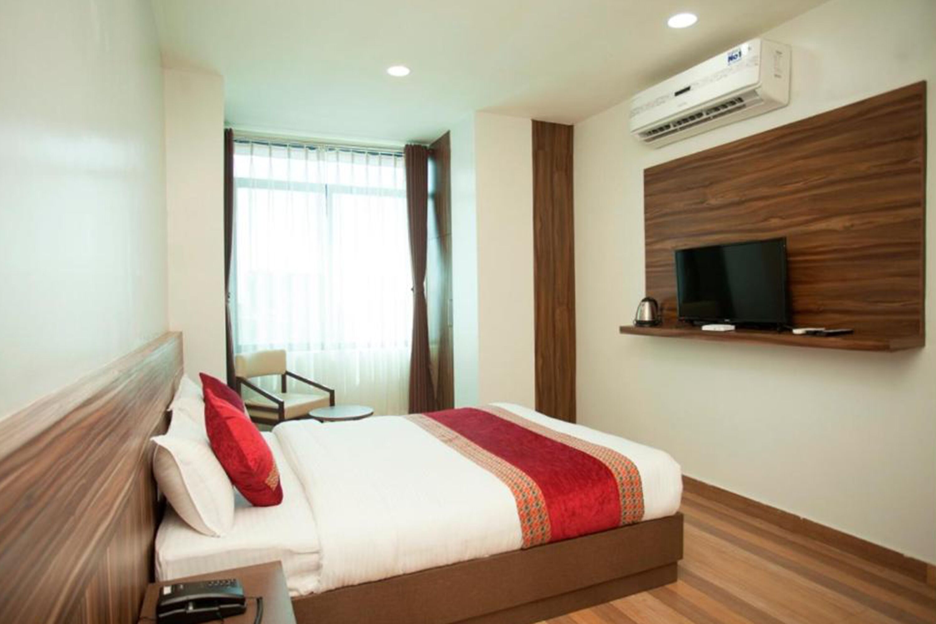 Una habitación de hotel con cama, televisión montada en la pared y aire acondicionado.
