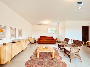 A modern living room with a wooden coffee table, wicker chairs, a red sofa, and a dining table.