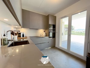 A modern kitchen with grey cabinets, stainless steel appliances, and a large window offering a view of the outdoors.
