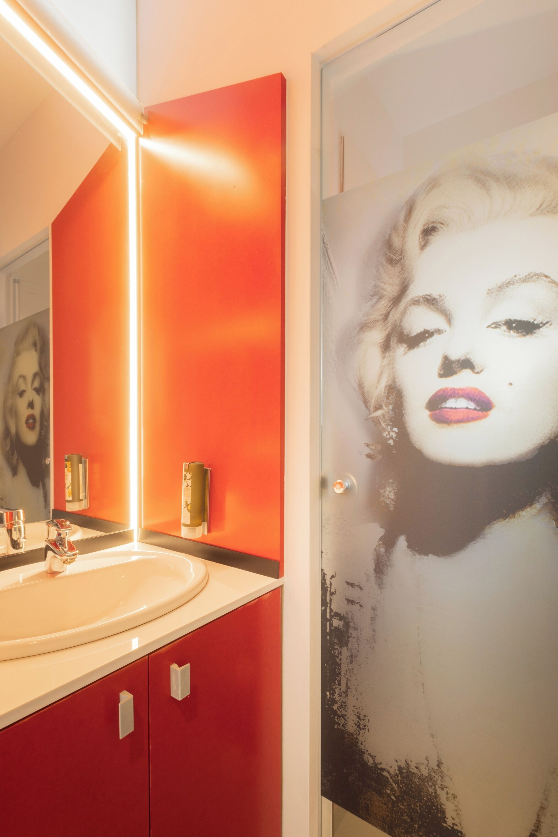A bathroom with a red wall, a white sink, and a mirror.