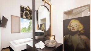 A hotel room with a bed, a round mirror, a stone sink, and a framed picture of a woman. - Das Edlinger (Salzburg)