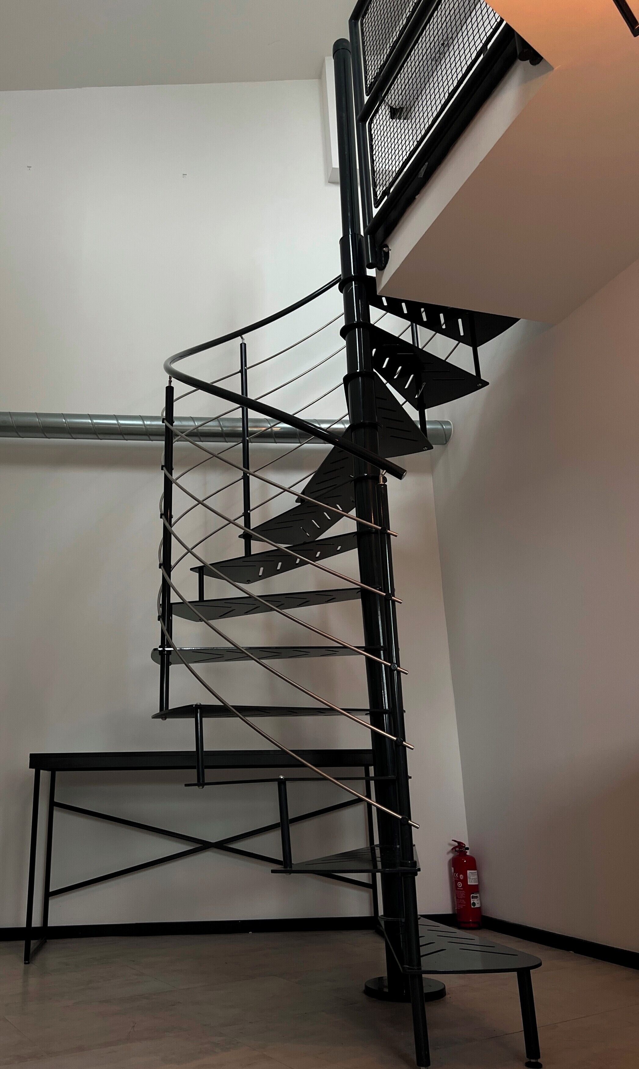 Eine schwarze Wendeltreppe mit Metallgeländern und einem Feuerlöscher auf dem Boden.