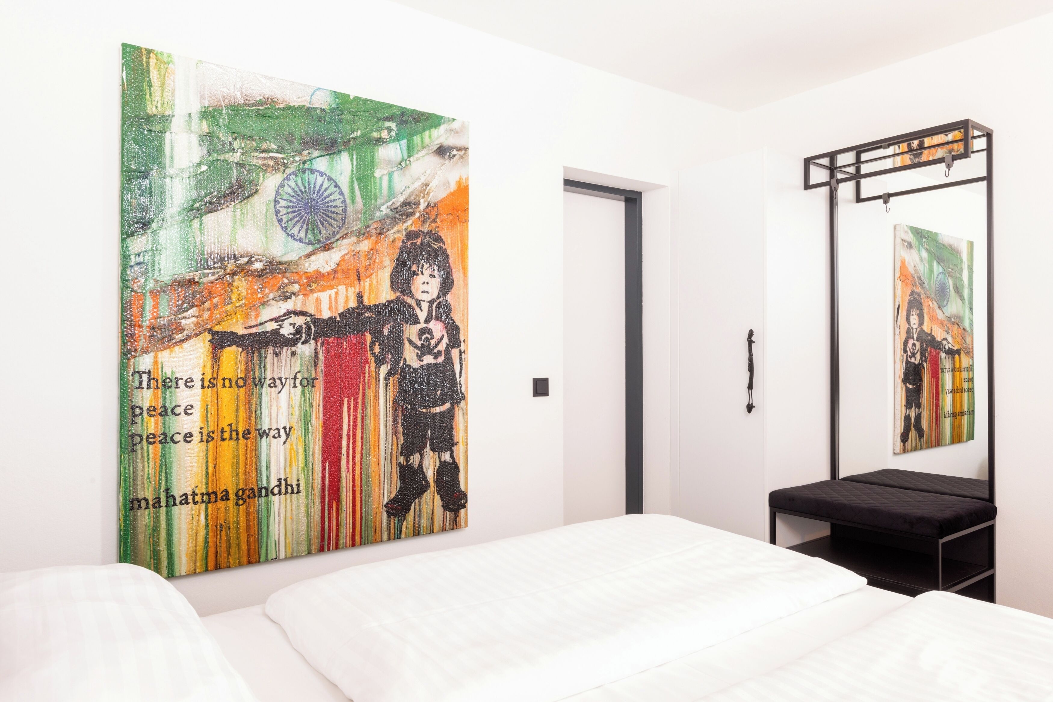 Una habitación de hotel moderna con un cuadro abstracto grande en la pared, una cama, un banco negro y un espejo.