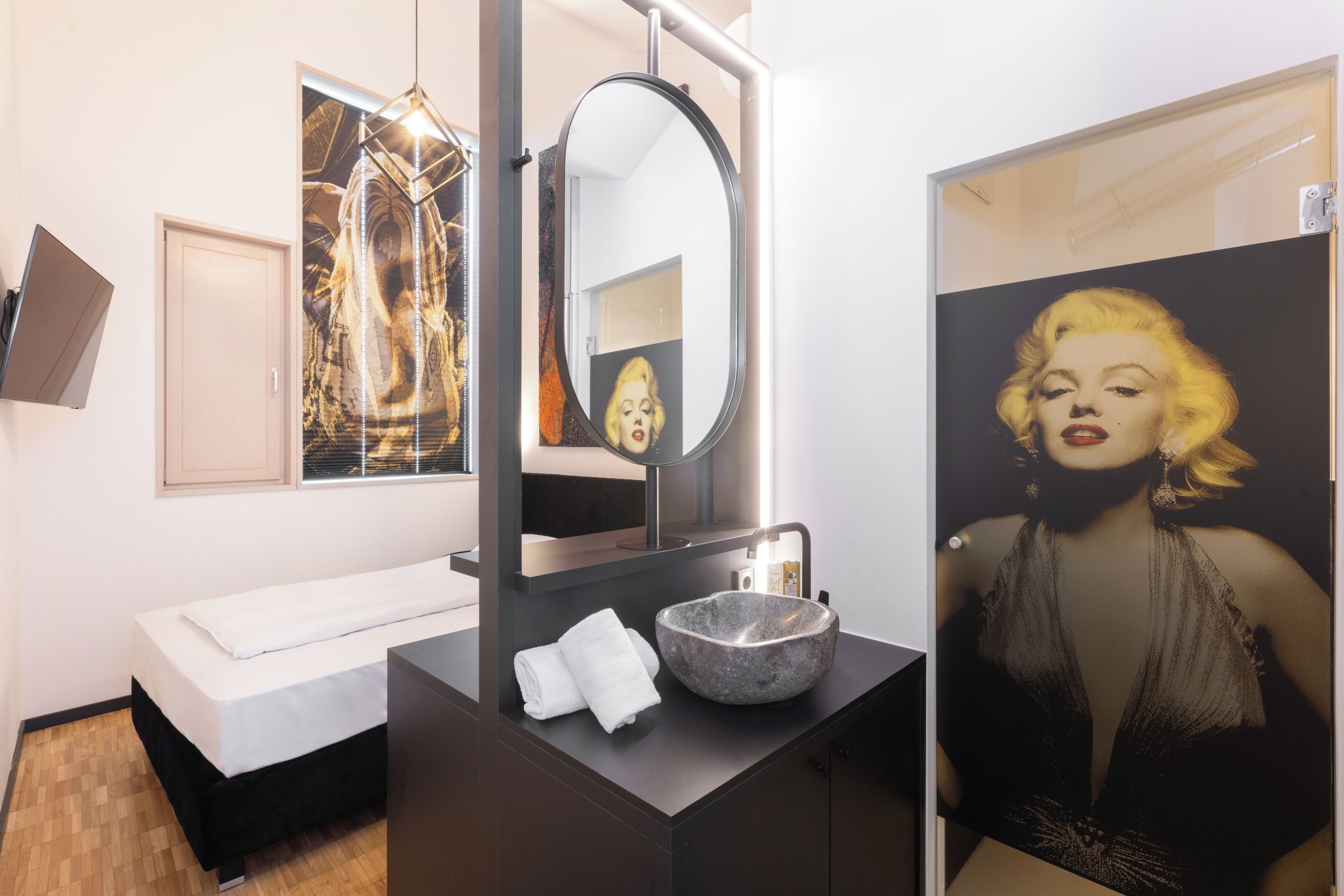 A modern bathroom with a large mirror, a sink with a stone basin, a white bench, and artwork on the walls.