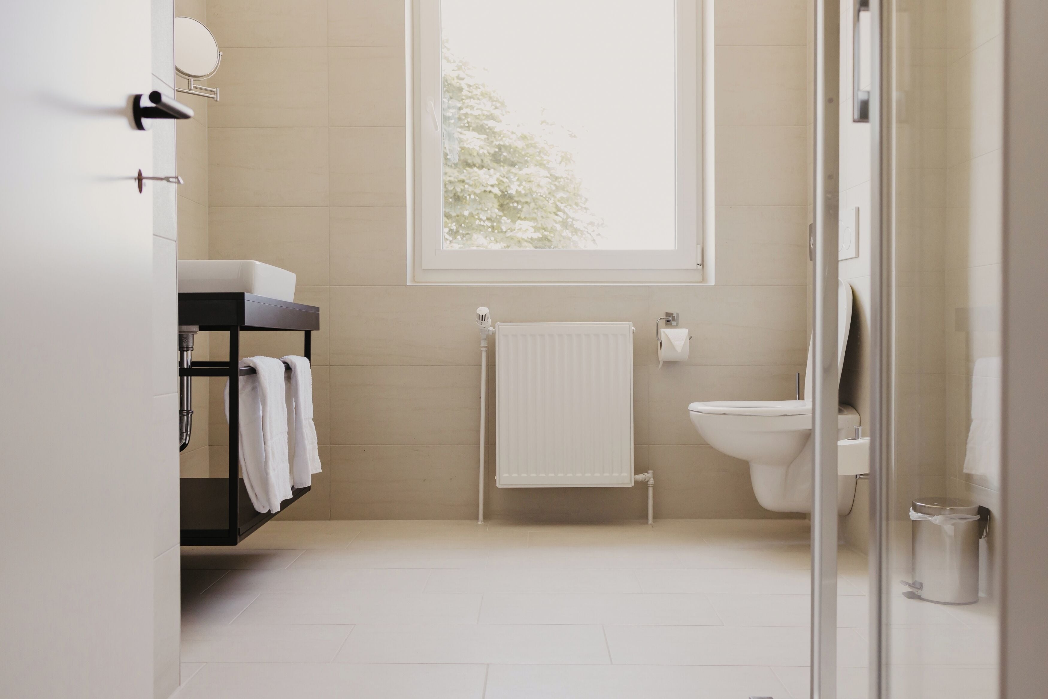 A modern bathroom with a glass shower door, a white toilet, and a black vanity with a towel rack.