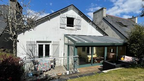 Een herenhuis met twee verdiepingen, een overdekte patio, een schoorsteen en een kleine tuin met potplanten.