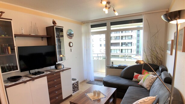 Una sala de estar moderna con una televisión de pantalla plana, una mesa de centro de madera, un sofá y un ventanal con vistas a la ciudad.