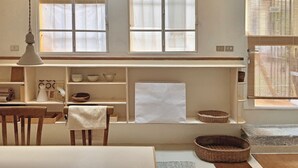 Un comedor con una mesa, sillas y una lámpara colgante. Hay estantes con cuencos y una cesta en el suelo.
