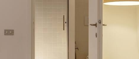 A hotel room with a shower area, a bed, and a lamp.