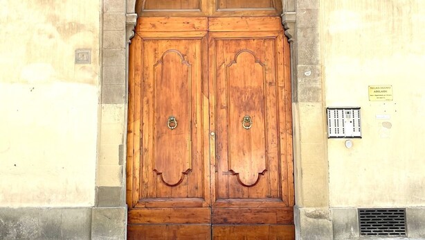 A large wooden double door with a stone archway, set in a building with a beige wall and a window above. - LEONARDO & DAVIDE APARTMENT FLORENCE, FREE WI-FI (Firenze)