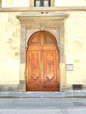 A large wooden double door with a stone archway, set in a building with a beige wall and a window above. - LEONARDO & DAVIDE Apartment in Florence, Free Wi-Fi (Firenze)