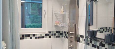 Un baño moderno con cabina de ducha de vidrio, un lavabo blanco con grifo cromado y un salpicadero de azulejos.