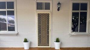 A house with a wooden porch, a welcome mat, and two potted plants.