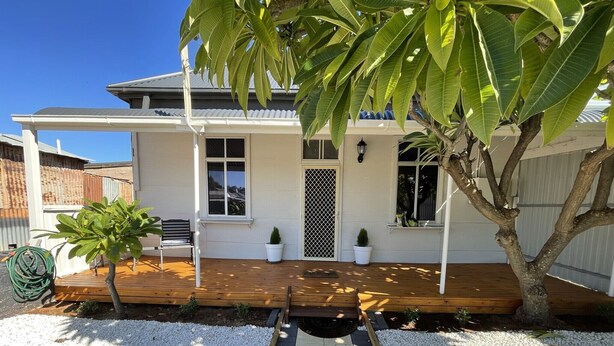 A house with a wooden deck, white walls, and a small garden with potted plants.