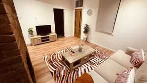 A living room with a sofa, a coffee table, a TV on a wooden stand, and a zebra-patterned rug.