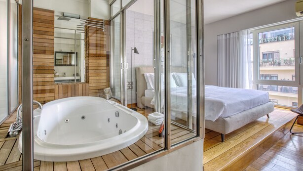 A modern hotel room with a large bathtub, a bed, and a balcony with a view. - Sunny Luxury Loft, Stunning Acropolis View, Jacuzzi (Athina)