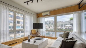 A modern living room with a large window, a flat-screen TV, a sofa, and a coffee table. - Sunny Luxury Loft, Stunning Acropolis View, Jacuzzi (Athina)