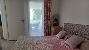 A bedroom with a patterned bedspread, a nightstand with a lamp, and a view of the outdoors through a door.