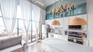 A modern kitchen with white cabinets, a large island, and a painting of sailboats on the wall.
