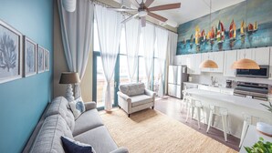 A modern living room with a sofa, a ceiling fan, and a painting of sailboats.
