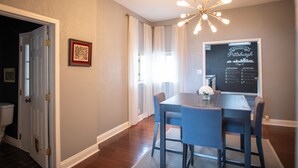 Zona pranzo con tavolo e sedie, un lampadario, un quadro incorniciato e una lavagna con un cartello di benvenuto.