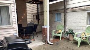 Un'area patio coperta con posti a sedere all'aperto, inclusi due poltrone verdi e un tavolo.