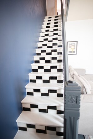 Un escalier à motifs à carreaux, menant à une pièce où se trouvent un lit et un tableau encadré au mur.