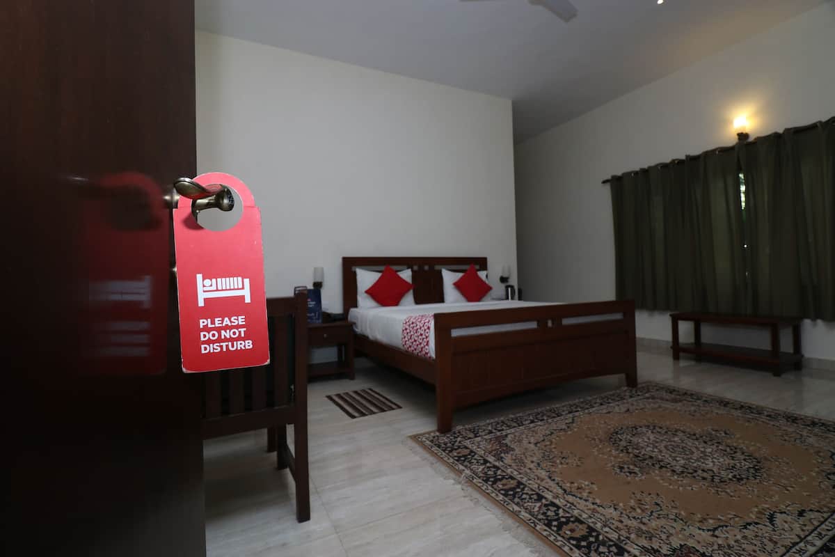 A bedroom with a bed, a nightstand, a bedside table, a wooden chair, a rug, and a sign on the door.