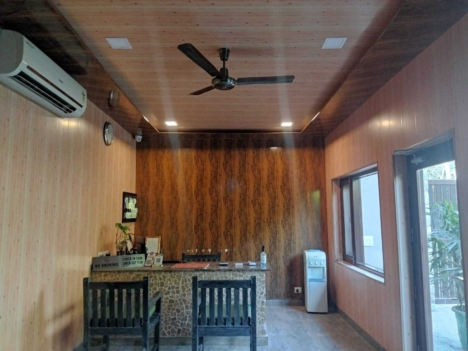 A room with a wooden ceiling, a ceiling fan, a stone counter, two wooden chairs, a refrigerator, and a window with a view of greenery outside.