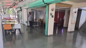 A spacious indoor area with a long corridor, a dining area with tables and chairs, and a person standing near the entrance. - Hotel Surya Villa (Pune)