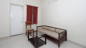 Una habitación con sofá, sillón, mesa de vidrio, ventilador de techo, puerta y cortinas rojas.