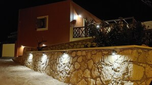 A stone wall with a balcony, a red building with a window, and a tree in the background.