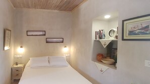A bedroom with a bed, bedside tables, a wall clock, framed pictures, and a shelf with books and a mirror.