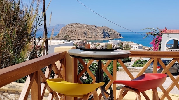 A balcony with a view of the sea, a mountain, and a building with a red roof.