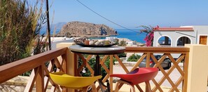 Un balcon avec vue sur la mer, une montagne et un bâtiment avec un toit rouge.