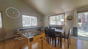 A cozy room with a foosball table, a dining table with chairs, and large windows. - 13 Timber-Sunriver, Oregon: Hot Tub, BBQ, WiFi, SHARC Aquatics, Tubing Hill, Mt. Bachelor, Golf, Deschutes River, Tennis, Bike Paths (Sunriver)