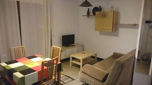 Een knus woongedeelte met een eettafel, stoelen, een bank, een televisie en een kast.