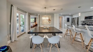 A modern kitchen with white cabinets, a large island with bar stools, and a dining area with a dark table and white chairs. - Villa Seafan - remodeld, new furniture, heated pool, kayaks, perfect for boaters (North Fort Myers)